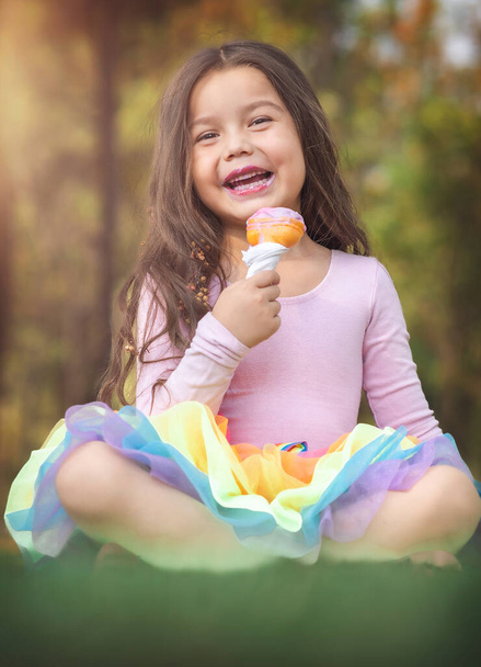 Schattig blond krullend meisje eet een lekker ijsje in het bos op een mooie zomerdag, kinderdagconcept, gelukkig meisje geniet van een warme dag. - Foto, afbeelding