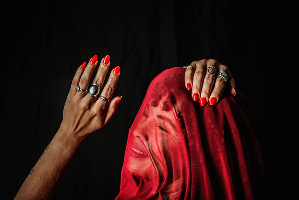 Beautiful woman with red cloth over her head making hand gestures. Isolated on black background. - Foto, Bild