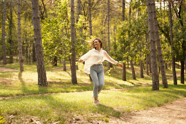 Экстатичная молодая женщина танцует в солнечном зеленом лесу, наслаждаясь свободой весной. - Фото, изображение
