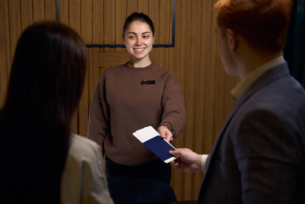 Przyjazny administrator rejestruje gości w recepcji, rudowłosy mężczyzna wręcza jej paszporty do rejestracji - Zdjęcie, obraz