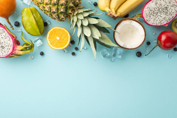 Tropical getaway concept. Top view of exotic dragon fruit, kiwi, pineapple, orange, carambola, tomatillo and coconut on a blue background with an empty space for promotional text - Photo, Image