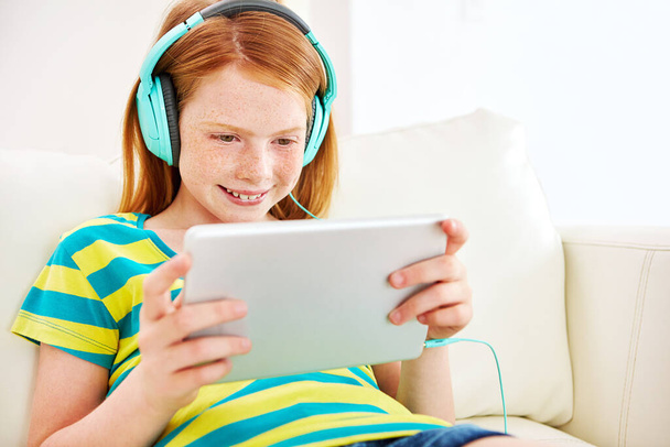Unterhalten mit einem animierten eBook. ein kleines Mädchen mit einem digitalen Tablet mit Kopfhörer zu Hause - Foto, Bild