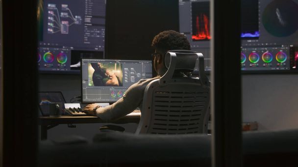 Doświadczony Afroamerykanin robi klasyfikację kolorów w programie na komputerze. Proces korekcji kolorystycznej postprodukcji filmowej w nowoczesnym studiu. Wielokrotne monitory z filmem akcji. - Zdjęcie, obraz