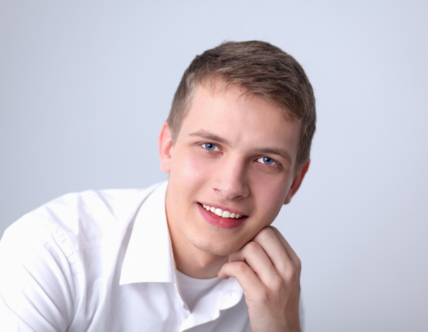 Portrait of young man smiling sitting on gray background - Foto, imagen