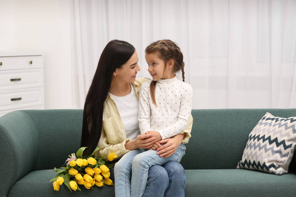 Szczęśliwa kobieta i jej urocza córka z bukietem żółtych tulipanów na kanapie w domu. Święto Dnia Matki - Zdjęcie, obraz