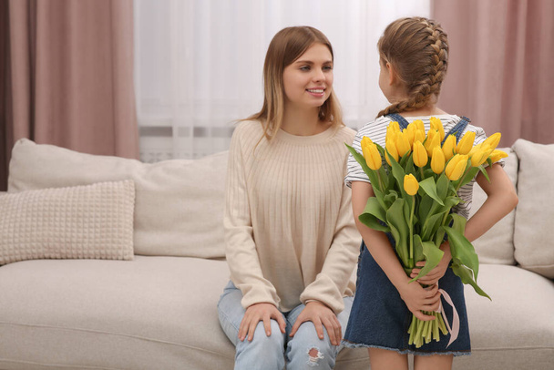 Little daughter congratulating mom with bouquet of yellow tulips at home. Happy Mother's Day - Valokuva, kuva