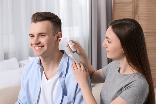 Woman spraying medication into man's ear at home - Foto, afbeelding