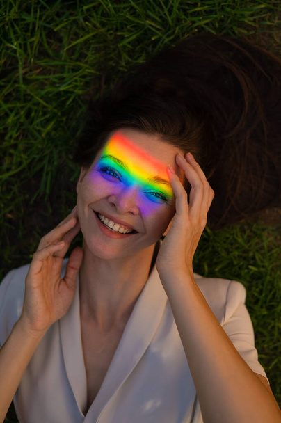 Top view of caucasian woman with rainbow ray on her face lies on green grass - Photo, image