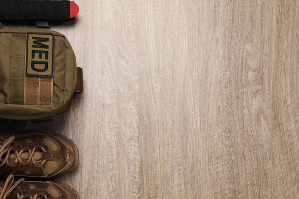 First aid kit and army boots on wooden table, flat lay. Space for text - 写真・画像