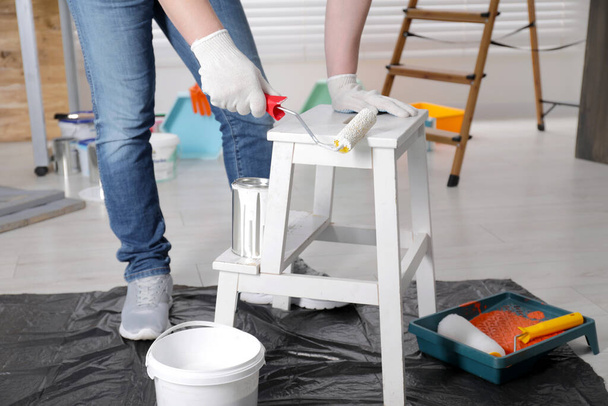Man using roller to paint bekvam with white dye indoors, closeup - Photo, image