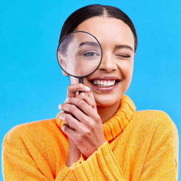 Smile, portrait and woman with a magnifier in a studio for an investigation or detective cosplay. Happiness, excited and headshot of a female model with a magnifying glass isolated by blue background. - Fotó, kép
