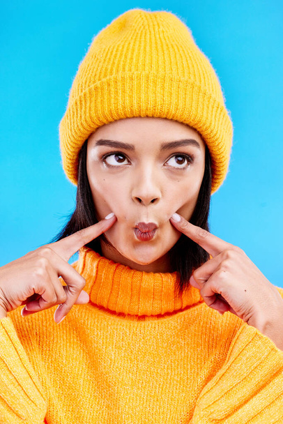 Goofy woman in winter fashion with comic expression, beanie and fun isolated on blue background. Style, happiness and silly gen z girl in studio with funny face and warm clothing for cold weather - Photo, image