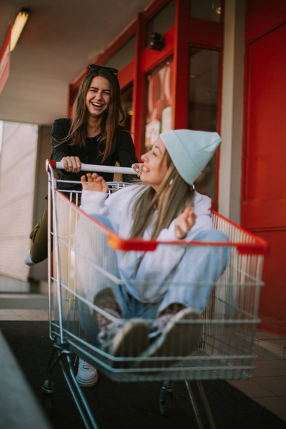 En iyi iki arkadaş alışveriş arabasıyla eğlenirken gülüyor. - Fotoğraf, Görsel