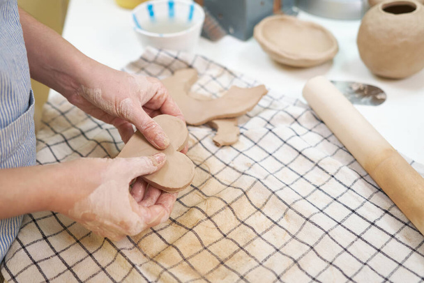Pottery female ceramist master in apron standing at work table in studio holding heart shaped piece of clay. - 写真・画像
