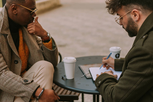 Close up shot of young businessman calculating monthly sales profit while having a coffee time with his black business partner - Zdjęcie, obraz