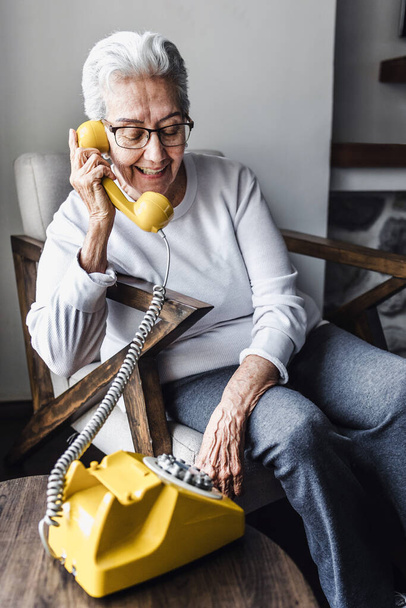 latin Grandmother or hispanic elderly woman talking by vintage phone at home in Mexico Latin America - Photo, Image
