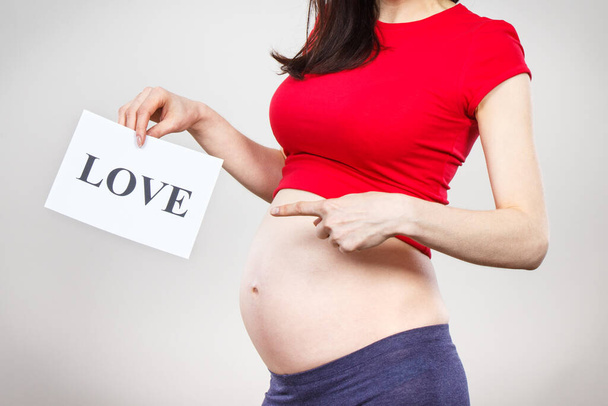 Woman in pregnant holding white card with inscription love. Expecting birth of newborn. Extending family. Motherhood - Foto, Imagem