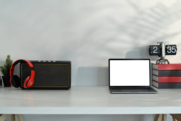 Laptop computer, wireless speaker, headphone and books on white table. Blank screen for advertising text message. - Photo, Image