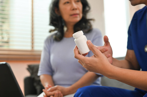 Health worker holding pills bottles explaining to senior patient. Medicine, healthcare and home health care service concept. - Photo, Image