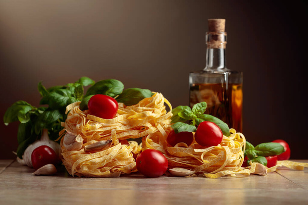 Kotitekoinen raaka pasta oliiviöljyllä, tomaatilla, valkosipulilla ja basilikalla ruskealla taustalla. Kopioi tila. - Valokuva, kuva