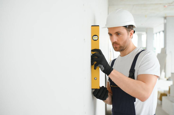 repair, building, technology and home concept - male with spirit level mesuring wall. - Foto, Imagem