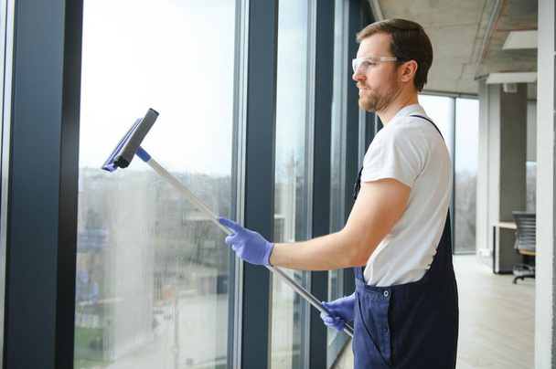 Ένας υπάλληλος μιας επαγγελματικής υπηρεσίας καθαρισμού πλένει τα τζάμια των παραθύρων του κτιρίου. Καθαρισμός βιτρίνας για καταστήματα και επιχειρήσεις - Φωτογραφία, εικόνα