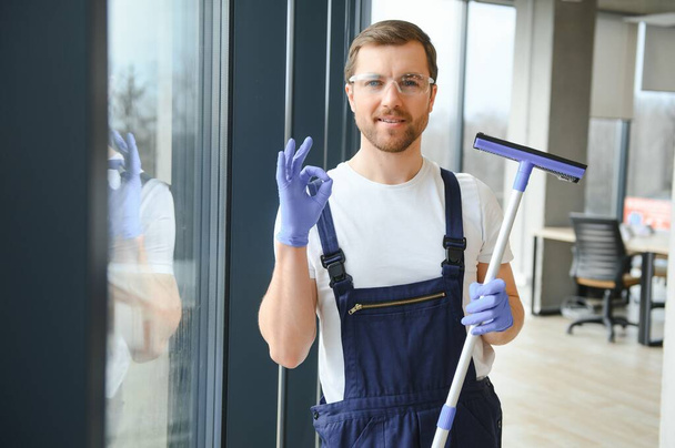 Male professional cleaning service worker in overalls cleans the windows and shop windows of a store with special equipment - Zdjęcie, obraz