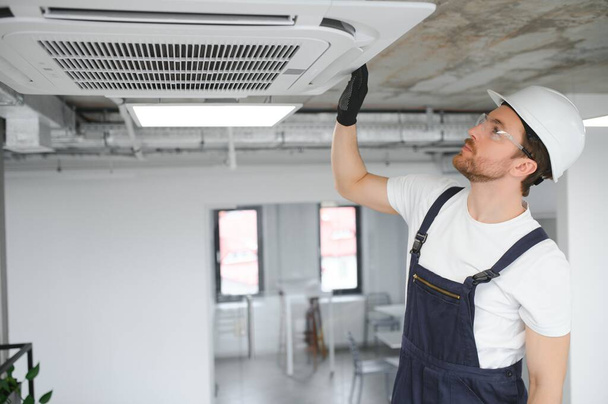 schöner junger Mann Elektriker installiert Klimaanlage in einem Kundenhaus - Foto, Bild