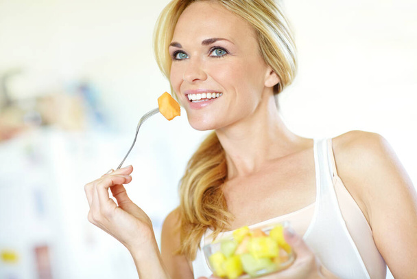 Eating right and enjoying it. Attractive young blonde woman enjoying a delicious fresh fruit salad at home - Foto, imagen