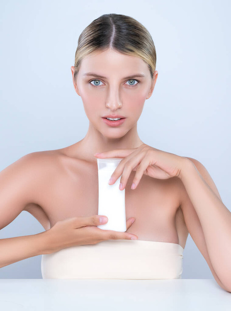 Intrygujący piękny idealny kosmetyk kobieta portret trzymać krem tubka makieta lub krem nawilżający do pielęgnacji skóry, anti-aging produktu w izolowanym tle. Naturalna koncepcja zdrowego modelu skóry. - Zdjęcie, obraz