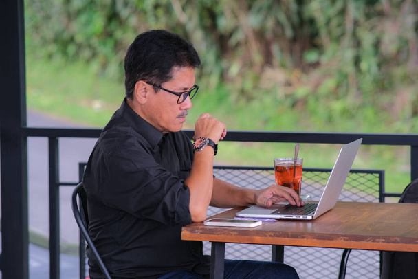 Asian man sitting alone and working on his laptop with lemon tea on the table - Foto, Imagen