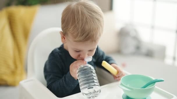 Schattige blonde peuter zit thuis op kinderstoel te eten snack drinkwater - Video
