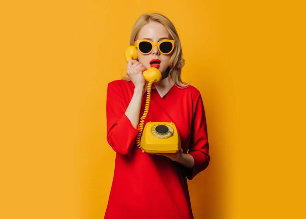 Stylish surprised woman in red dress with dial phone on yellow background - Zdjęcie, obraz