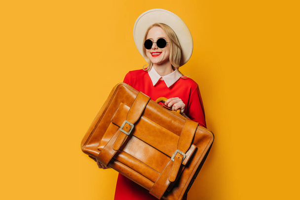 笑顔ブロンド髪の女性で赤ドレススーツケースとともに黄色の背景 - 写真・画像