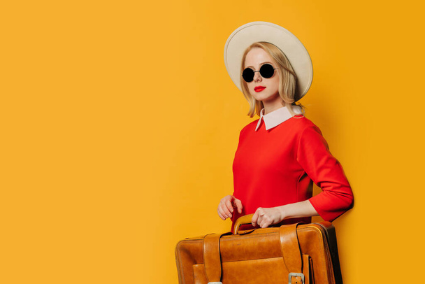 Stylish blonde hair woman in red dress with suitcase on yellow background - Foto, immagini