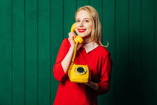 Stylowa blondynka włosy kobieta w czerwonej sukience z telefonem na zielonym drewnianym tle - Zdjęcie, obraz
