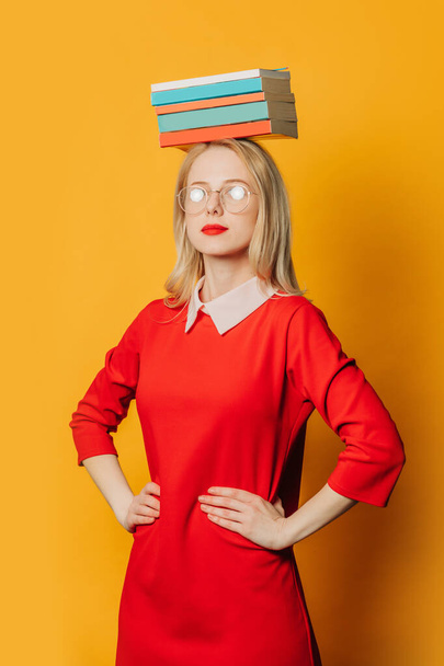 Stylish blond hair woman in glasses and red dress with book on head on yellow background - Foto, Imagem