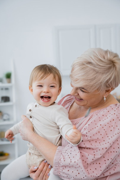 радісна дівчинка тримає ложку біля усміхненої бабусі на кухні. - Фото, зображення