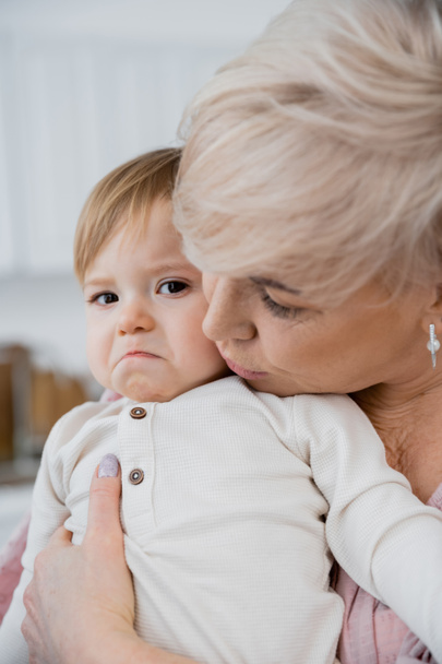 abuela calmar y abrazar molesto bebé niña en casa - Foto, imagen