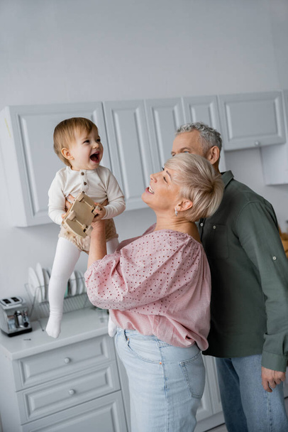 збуджена дівчина з іграшковою машиною сміється біля щасливих бабусь і дідусів на кухні
 - Фото, зображення