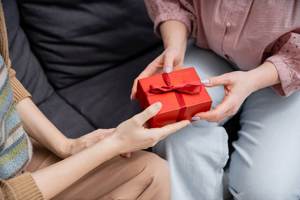 cropped view of woman presenting gift to mature mother on couch at home - Foto, Bild