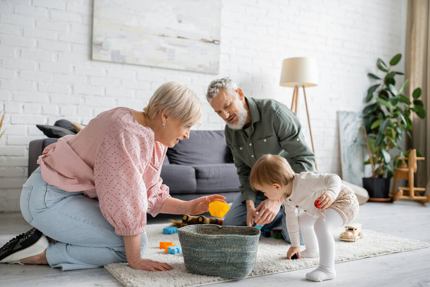 para w średnim wieku gra z wnuczką malucha na podłodze dywan w nowoczesnym salonie - Zdjęcie, obraz