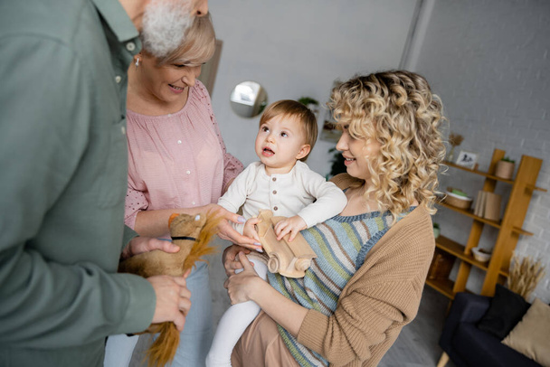 здивована дівчина дивиться на бабусь і дідусів біля щасливої кучерявої матері у вітальні
 - Фото, зображення