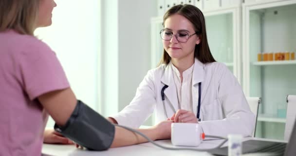 Il medico in occhiali misura la pressione sanguigna della paziente con sfigmomanometro. Specialista fa esame della salute della donna in clinica rallentatore - Filmati, video