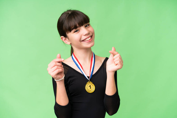 Маленькая кавказская девочка с медалями на изолированном фоне зарабатывает деньги жест - Фото, изображение