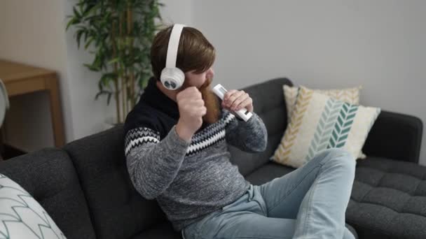 Young redhead man listening to music singing song at home - Video