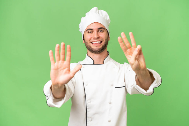Junger gutaussehender Koch über isolierten Hintergrund, der mit den Fingern acht zählt - Foto, Bild