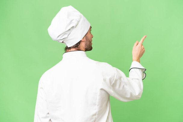Young handsome chef man over isolated background pointing back with the index finger - Φωτογραφία, εικόνα