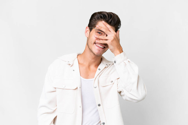 Young handsome caucasian man over isolated white background covering eyes by hands and smiling - Fotó, kép