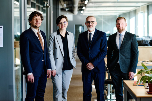 Portret van succesvol business team in formele kleding kijkend naar camera terwijl ze op kantoor staan - Foto, afbeelding
